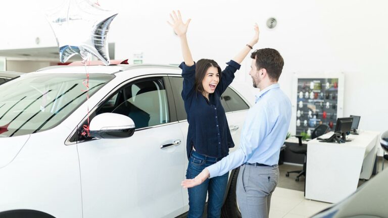 Woman excitedly throwing her arms in the air next to a new car