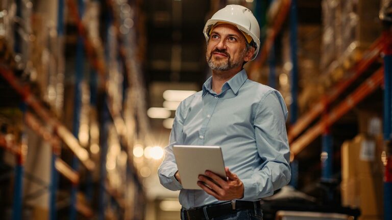 Man in a hard hat looking over inventory in a warehouse